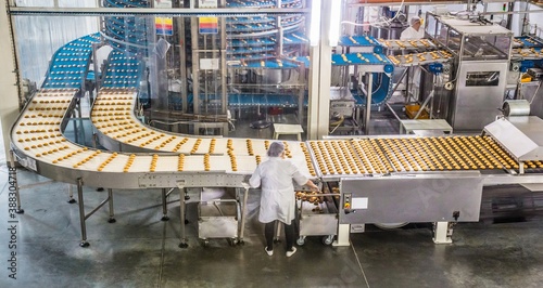 ULYANOVSK, RUSSIA - APRIL 19, 2017. Women in uniform controlling the work of huge conveyor machine producing spice cakes at the confectionary plant.