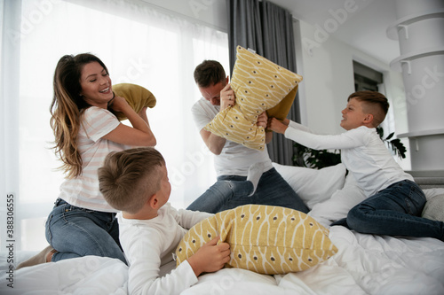 Young parents with sons fighting pillows on the bed. Happy mother and father with boys having fun at home.. photo