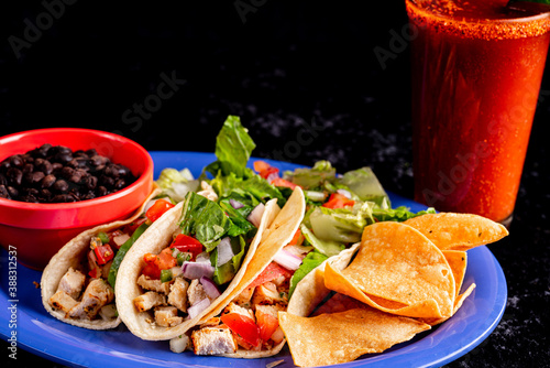 A delicious plate of tacos with a flavorful beverage, beans and salad.