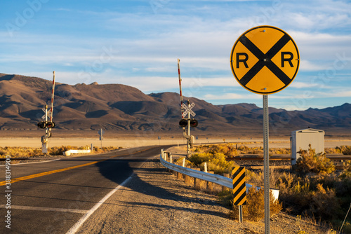 Image of a railroad crossing at the intersection of a highway in a mountainous desert