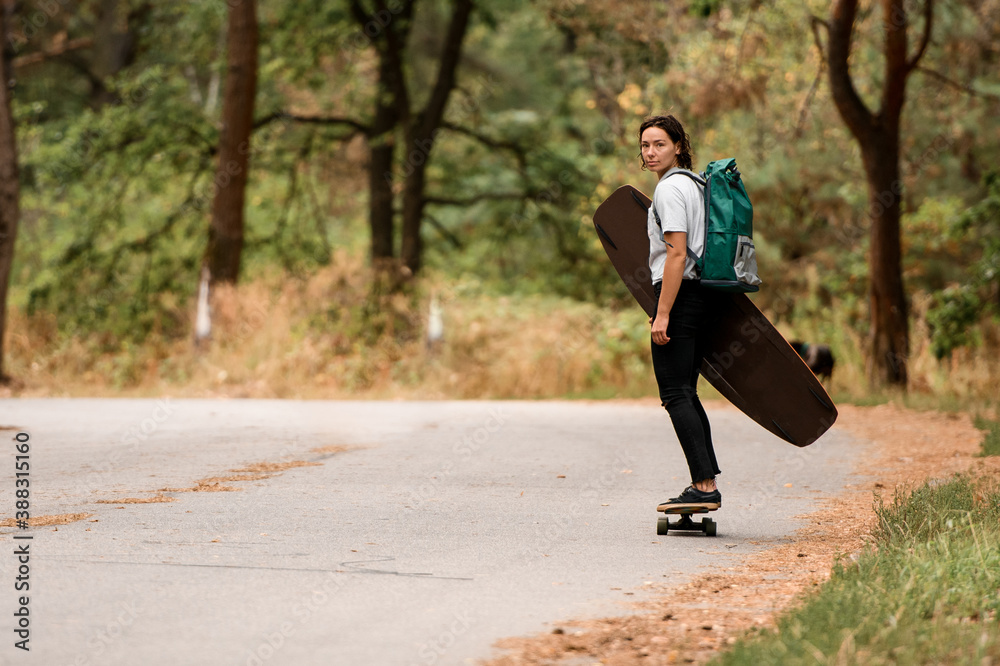 young sportive woman riding skateboard with wakeboard in her hand and backpack on her shoulders. young sportive woman riding skateboard with wakeboard in her hand and backpack on her shoulders.