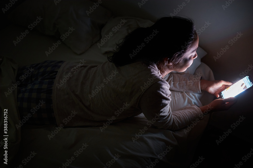 Mujer joven acostada en su cama texteando y navegando por la web en la noche