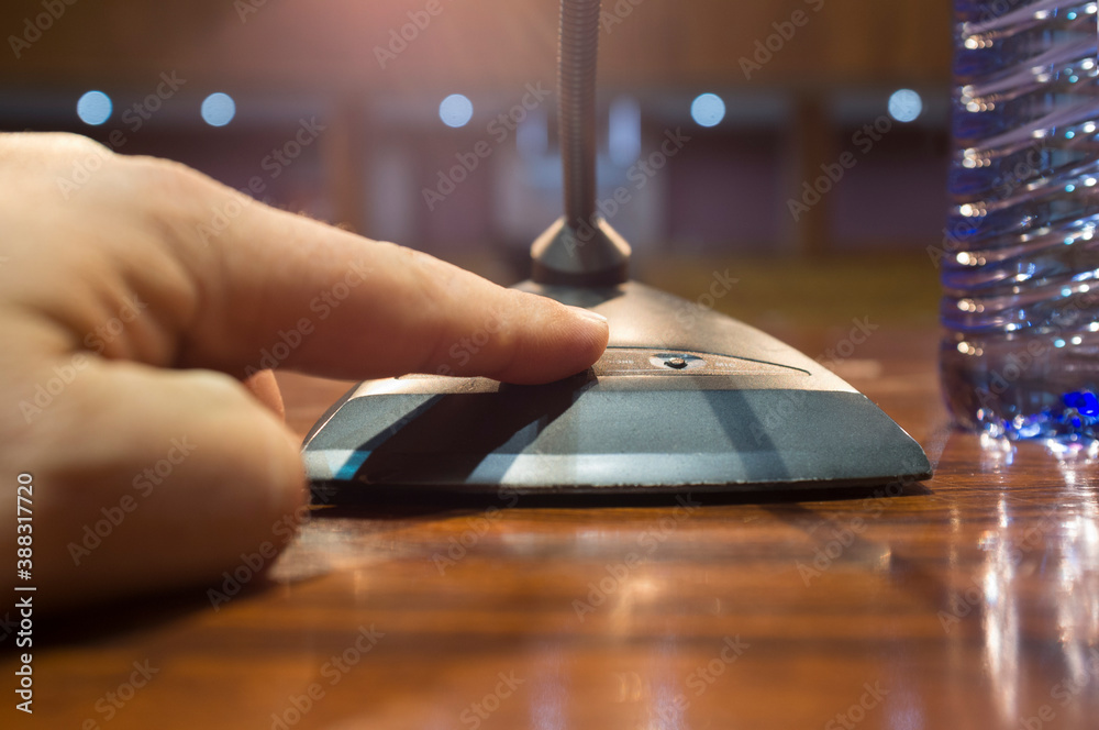 Obraz premium Speaker finger is about to press on-off button of a table conference microphone