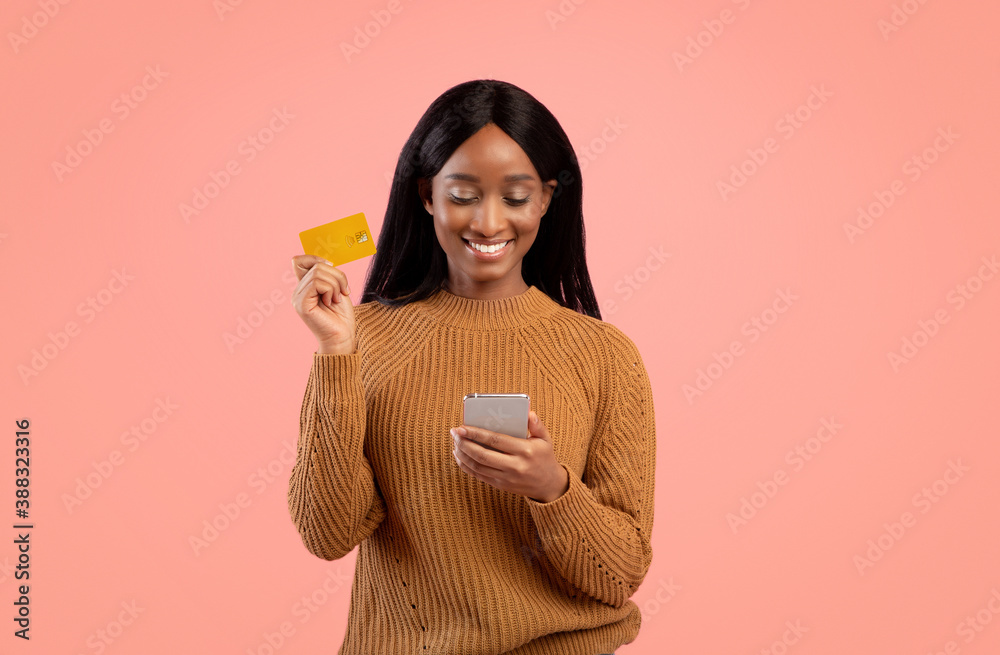 Internet shopping. Positive black woman with cellphone and credit card purchasing things online over pink background Internet shopping. Positive black woman with cellphone and credit card purchasing things online over pink background