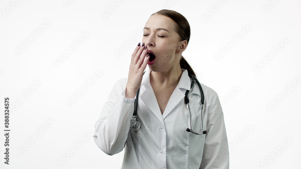 Young beautiful female doctor in medical uniform feels tired, yawns, put on portable travel neck pillow for nap or snooze and closed her eyes, isolated white background. Overworking, medical concept Young beautiful female doctor in medical uniform feels tired, yawns, put on portable travel neck pillow for nap or snooze and closed her eyes, isolated white background. Overworking, medical concept
