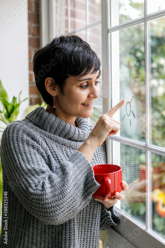 young relaxed woman at home by the window holding a cup of tea or coffee. autumn or winter season