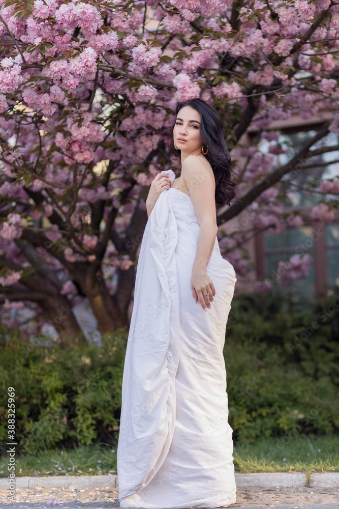 people, rest, comfort and leisure concept - Young woman through the evening streets wrapped in a blanket. Beautiful young girl in the park and a flowering tree sakura