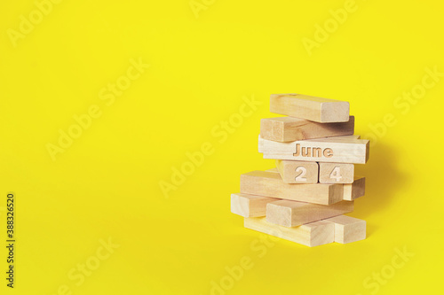 June 24th. Day 24 of month, Calendar date. Wooden blocks folded into the tower with month and day on yellow background, with copy space. Summer month, day of the year concept.