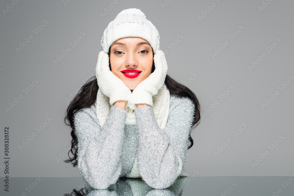 joyful and brunette woman in winter outfit looking at camera isolated on grey