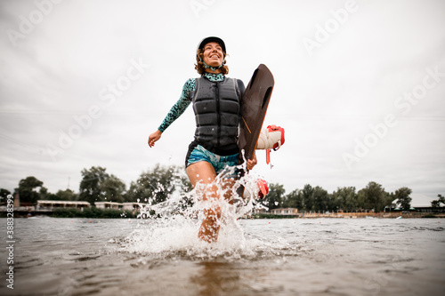 Fototapeta Naklejka Na Ścianę i Meble -  cheerful young woman with helmet and wakeboarding board runs out of the water