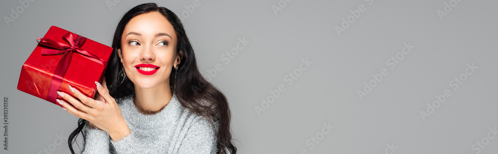 happy woman with red lips holding present isolated on grey, banner