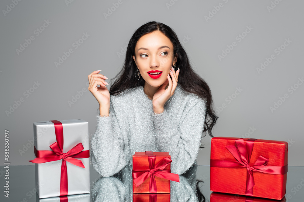 Fototapeta premium happy woman with red lips looking away near gift boxes isolated on grey