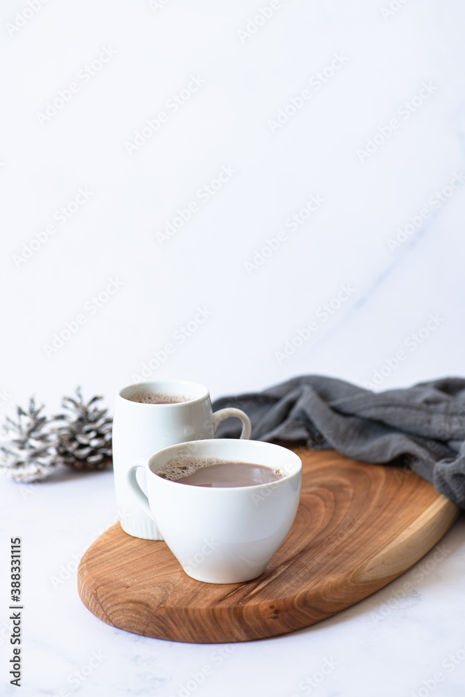 Two white cups with hot chocolate or cocoa drink on a wooden board on a light marble background with festive winter decorations. Winter mood. Frontal view. Copy space. Selective focus