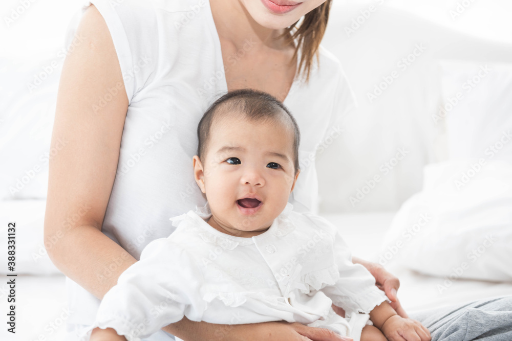 Asian mother and baby laugh together at home. Asia mom holdind infant and sitting on white bed in living room at house  having fun together.