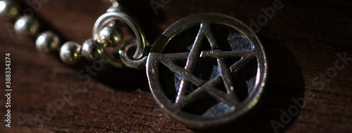 Obraz na plátně Silver Pentagram charm old necklace on a dark brown wooden surface, light and sh