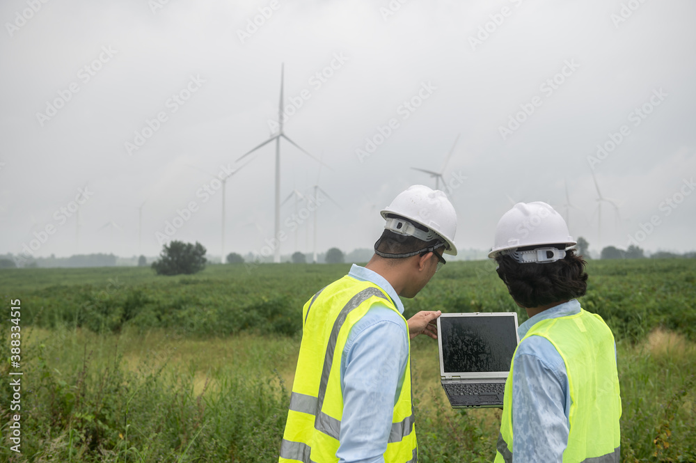 Two engineers working and holding the report at wind turbine farm Power Generator Station on mountain,Thailand people Two engineers working and holding the report at wind turbine farm Power Generator Station on mountain,Thailand people