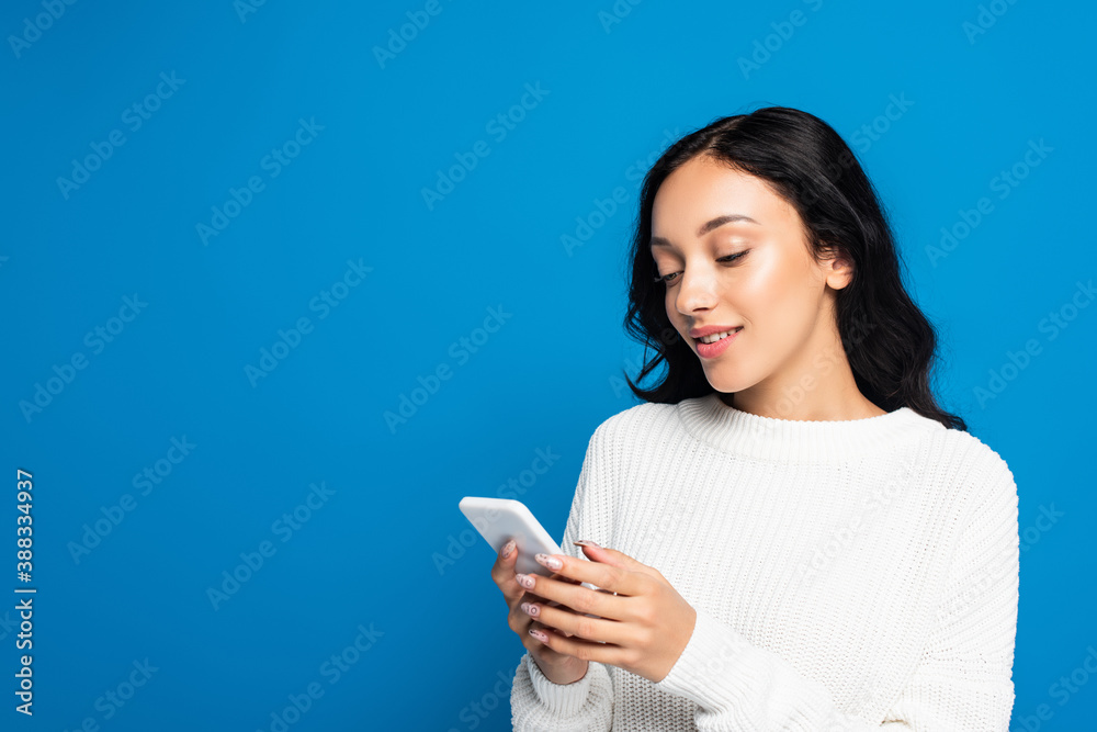 young woman in warm sweater using smartphone isolated on blue young woman in warm sweater using smartphone isolated on blue