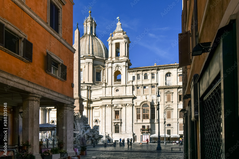 View of the  Sant'Agnese in Agone church, the Fountain of the Four Rivers with obelisk and tourists in silhouette from an alleyway leading to the Piazza Navona in Rome Italy.