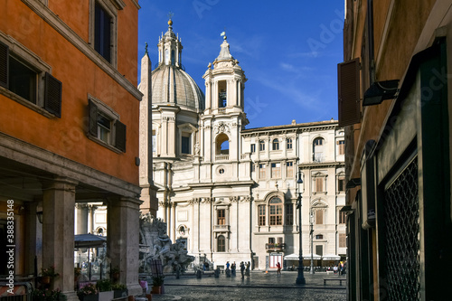 View of the Sant'Agnese in Agone church, the Fountain of the Four Rivers with obelisk and tourists in silhouette from an alleyway leading to the Piazza Navona in Rome Italy.
