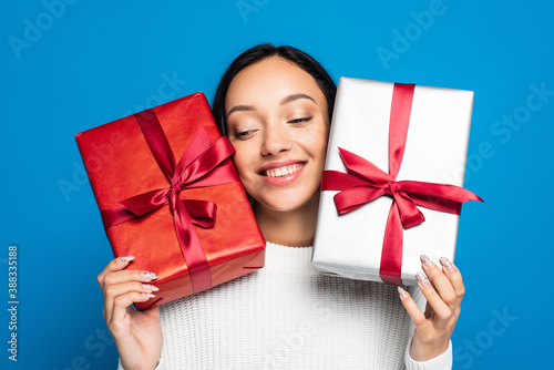 pleased young woman in knitted sweater holding gift boxes isolated on blue © LIGHTFIELD STUDIOS