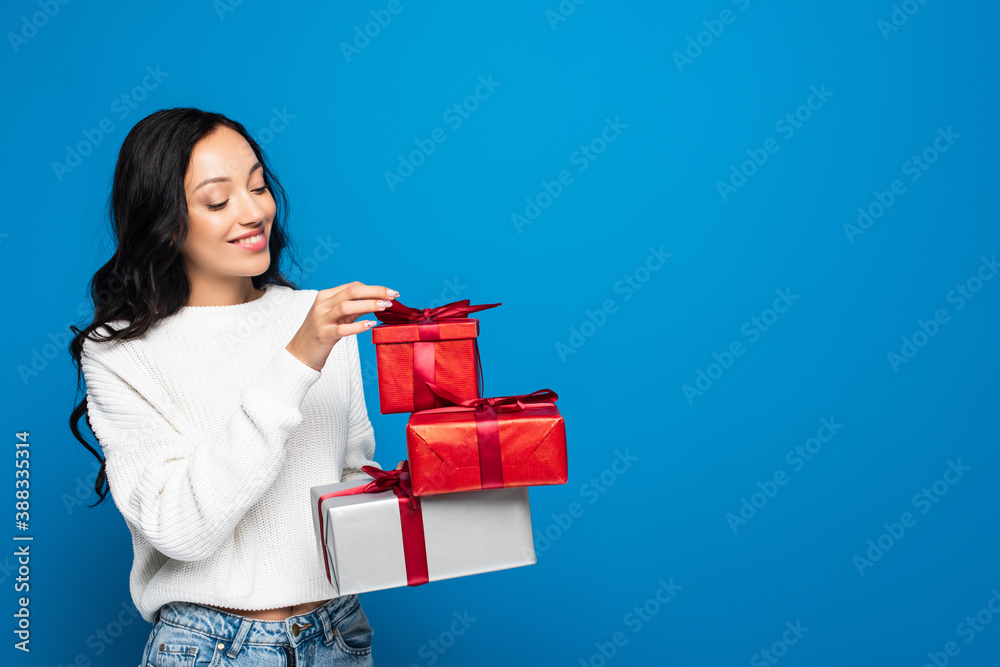 cheerful young woman in knitted sweater holding gift boxes isolated on blue cheerful young woman in knitted sweater holding gift boxes isolated on blue