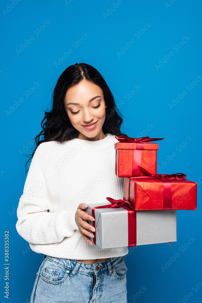 happy young woman in knitted sweater holding gift boxes isolated on blue happy young woman in knitted sweater holding gift boxes isolated on blue