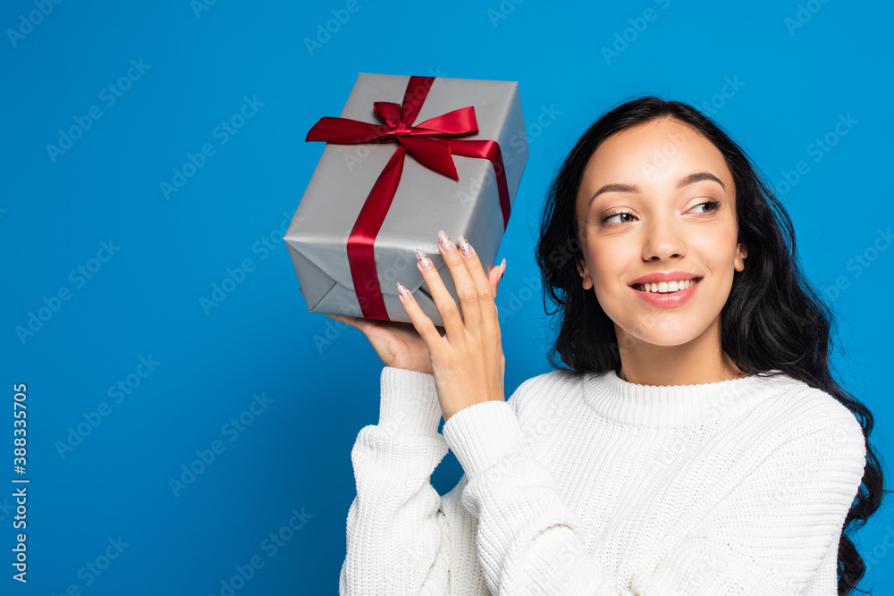 happy woman in knitted sweater holding gift box isolated on blue happy woman in knitted sweater holding gift box isolated on blue