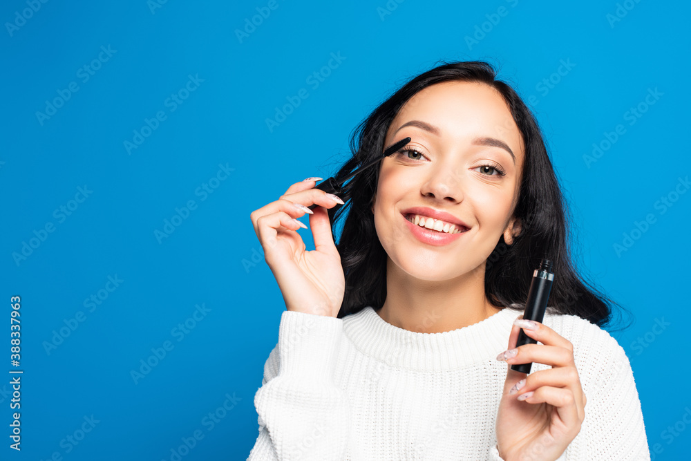 happy brunette woman applying mascara isolated on blue happy brunette woman applying mascara isolated on blue