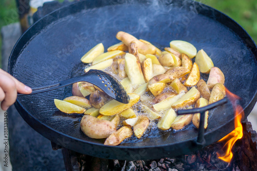 the cook stirs the potatoes which are fried on an open fire in oil, copy space. out of doors