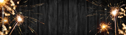 Silvester / New Year background banner panorama - sparklers firework and bokeh lights on rustic black wooden texture, with space for text