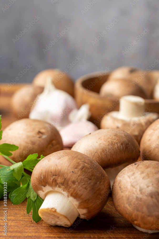 Top view of portobello mushrooms, garlic and parsley, with selective focus, on wooden board, gray background, vertical