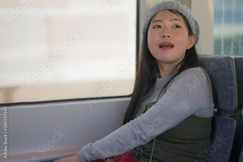 lifestyle portrait of young happy and beautiful Asian Korean woman excited and cheerful looking through window sitting on train enjoying landscape from the railcar glass