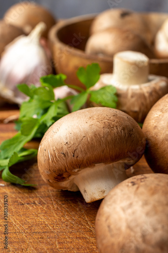 Close-up of portobello mushrooms, garlic and parsley, with selective focus, on wooden board, in vertical photo