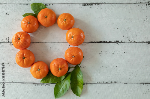 Tangerines with leaves in the form of a Christmas wreath on a background of white wooden boards. The view from the top. Christmas cards and decorations.