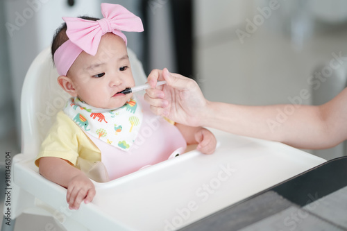 Asian cute baby girl taking a liquid drug after a meal. Her mother is injecting a black syrup medicine, iron in syringe to prevent iron deficiency mostly found in baby
