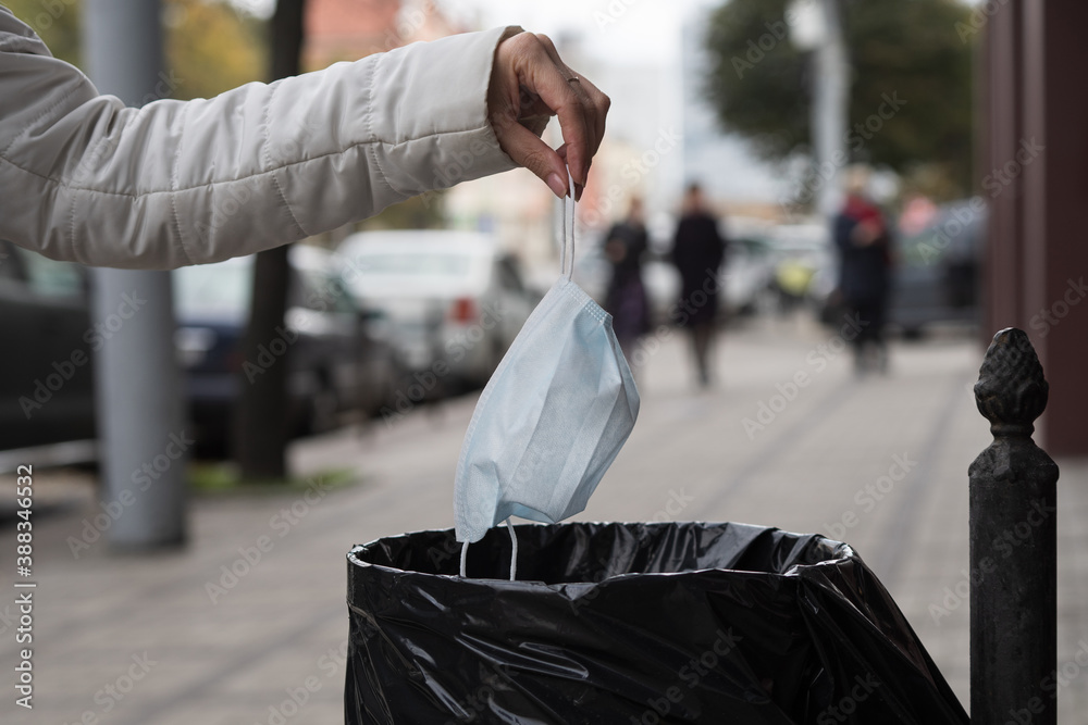 Obraz premium A woman throws a facemask at a public trash can on a city street.