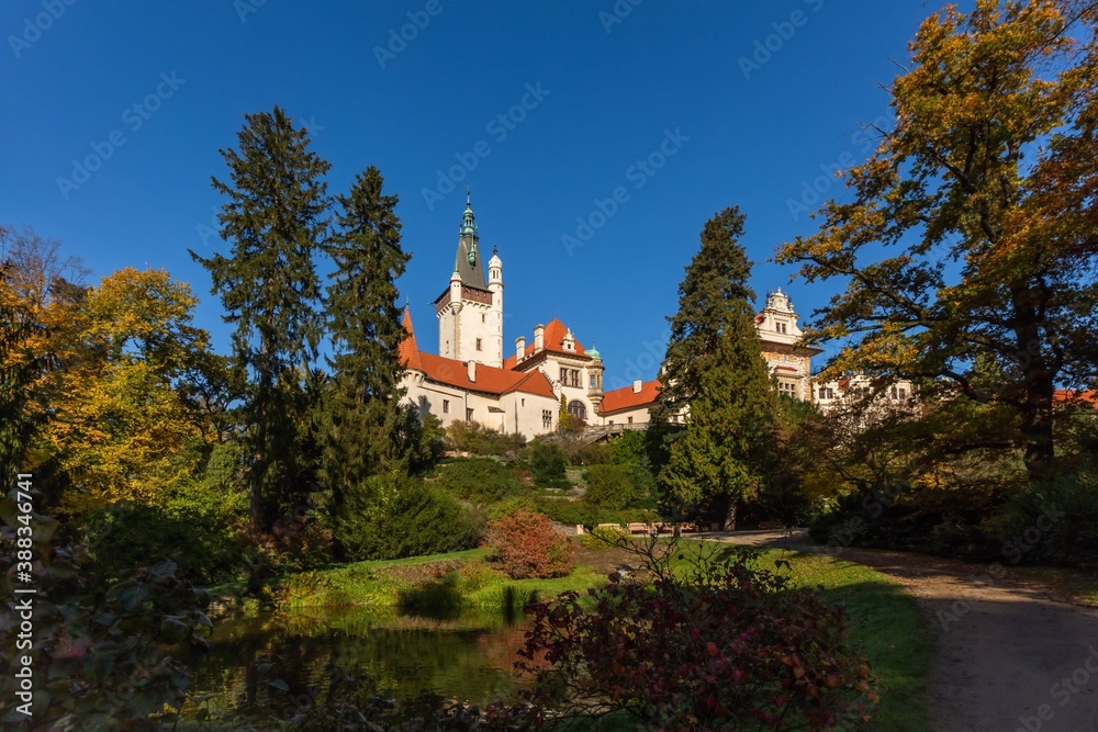Pruhonice, Czech Republic - October 25 2020: Scenic view of famous romantic castle standing on a hill in a park surrounded with green trees. Sunny autumn day with clear blue sky. 