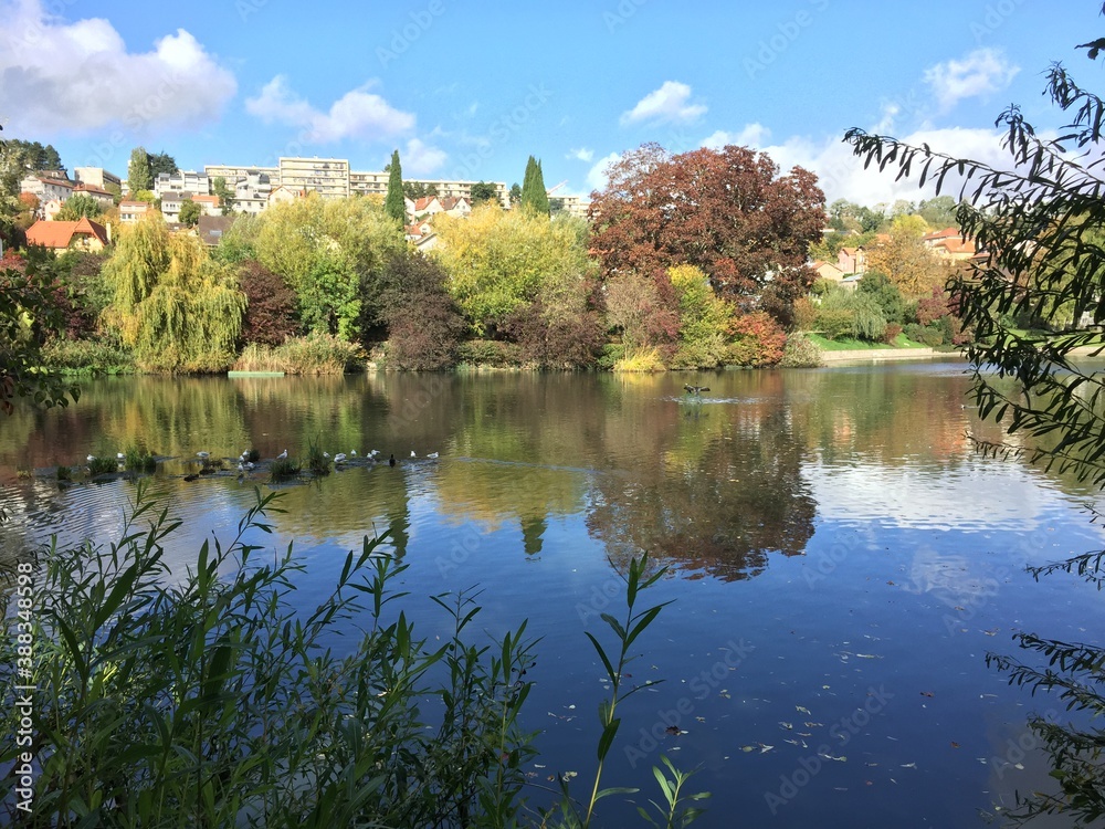 Vue d'un étang en ville par temps ensoleillé, avec reflets des nuages dans l'eau