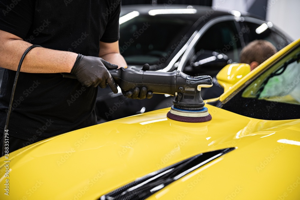 Man car detailing studio worker polishing yellow car varnish with electrical polisher