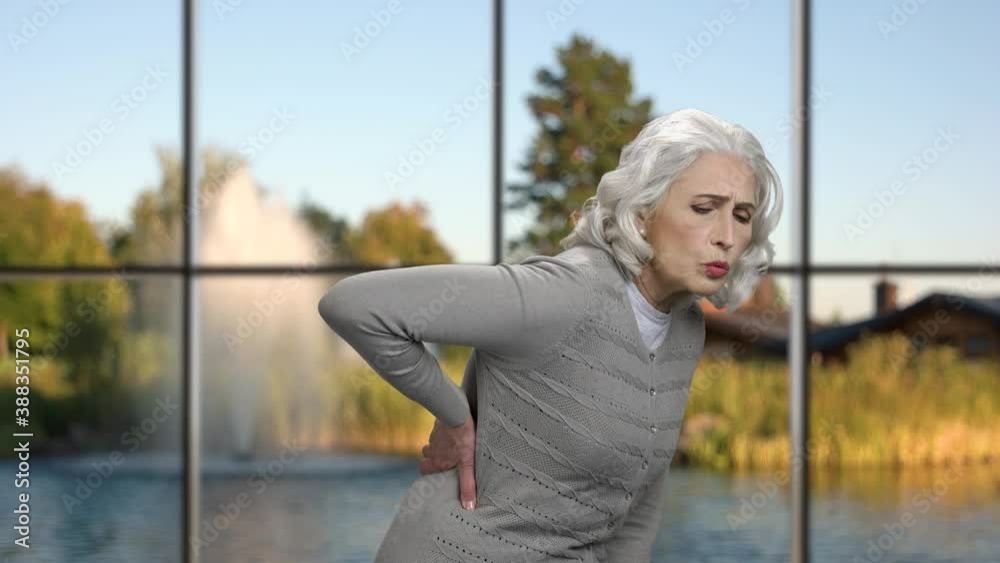 Unhappy mature woman suffering from back pain. Woman having back ache against windows with beautiful nature view. Unhappy mature woman suffering from back pain. Woman having back ache against windows with beautiful nature view.