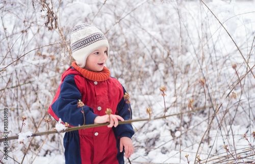 A little boy in a winter jumpsuit in a snowy wild field. Boy in warm winter clothes