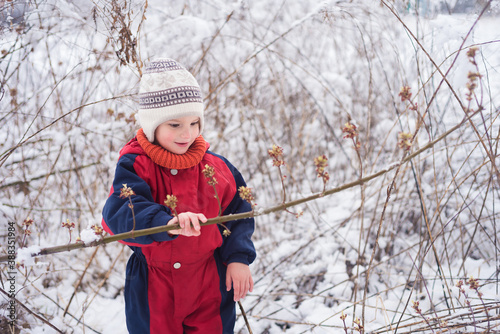 A baby in a warm winter cobineson looks at a branch of dryness in a wild park