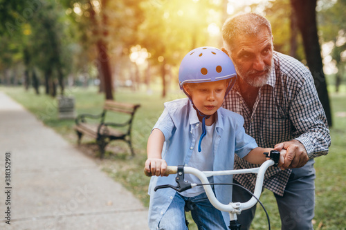 boy learning to ride a bike with his grandfather in park