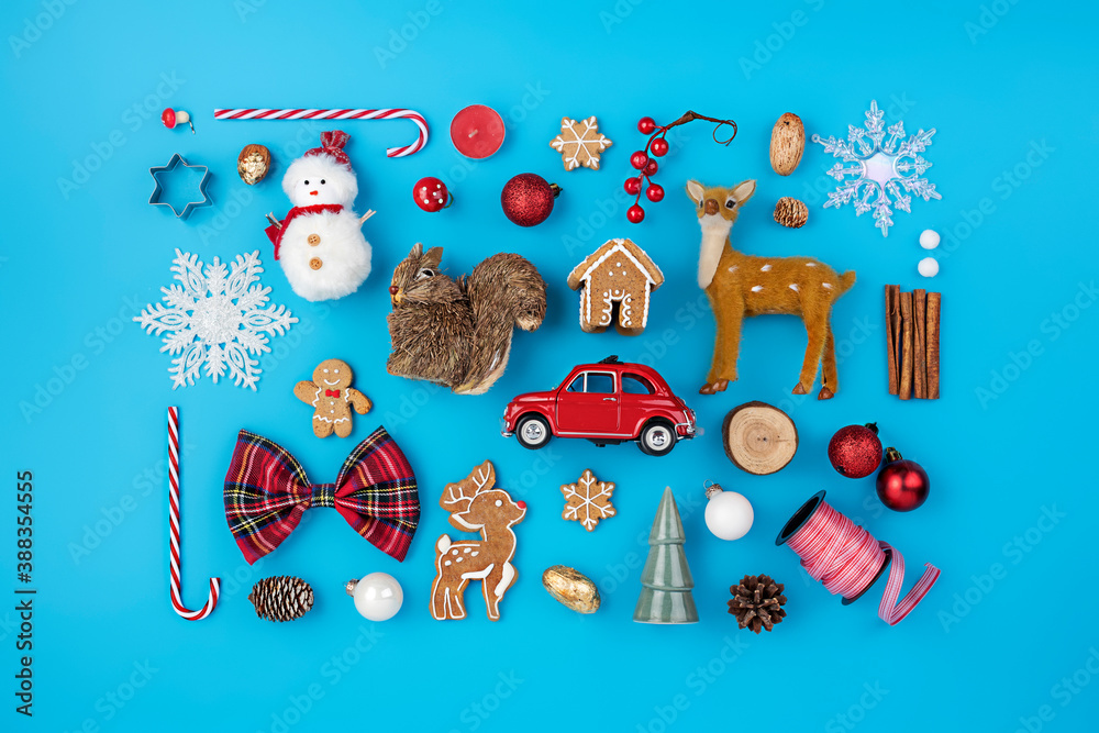 Naklejka premium Christmas holiday decorative layout made with candy cane, ornaments, snowman, deer and gingerbread man on blue background. Minimal winter or New Year concept with copy space. Flat lay, top view.