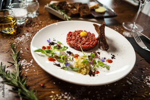 Steak tartare. Horseradish creme, black bread, baguette chips on white plate. Delicious healthy raw meat food closeup served on a table for lunch in modern cuisine gourmet restaurant.