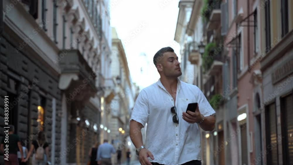 Handsome man in casual clothes walking along the beautiful crowded street with smartphone in hands, young male looking at magnificent building exterior and enjoying afternoon stroll. Person using Handsome man in casual clothes walking along the beautiful crowded street with smartphone in hands, young male looking at magnificent building exterior and enjoying afternoon stroll. Person using