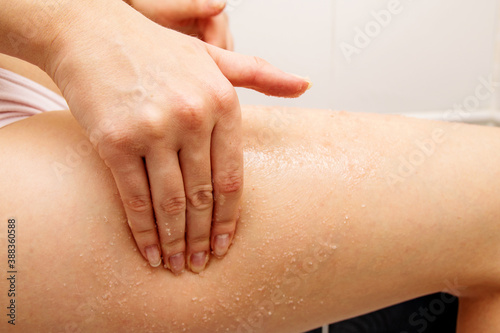 In the frame  the girl s hand scrubs the skin of her thigh with salt for massage