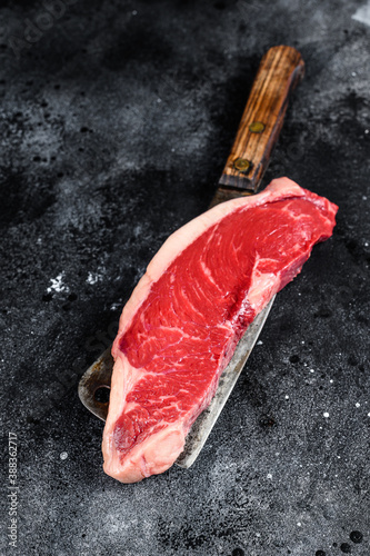 Raw strip loin steak on a cleaver. Black Angus beef. Black background. Top view