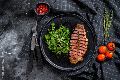Sliced sirloin steak, marbled beef meat with arugula. Black background. Top view