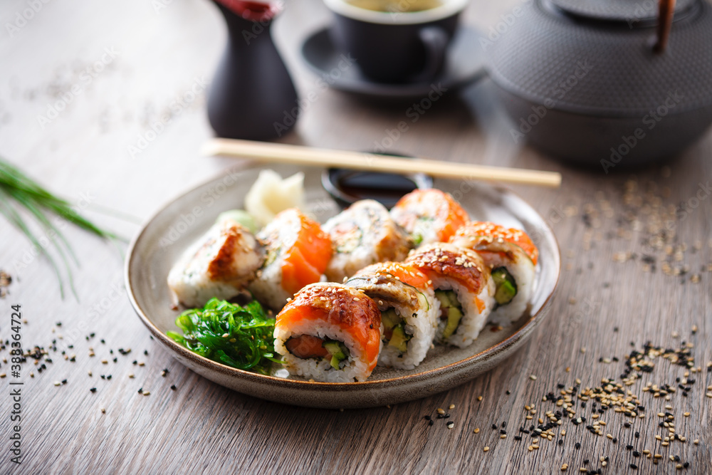 Sushi maki rolls with salmon, eel, avocado, cucumber on a plate with chopsticks, soy sauce, wasabi and ginger. Japanese traditional fish food closeup served for lunch in modern gourmet restaurant Sushi maki rolls with salmon, eel, avocado, cucumber on a plate with chopsticks, soy sauce, wasabi and ginger. Japanese traditional fish food closeup served for lunch in modern gourmet restaurant